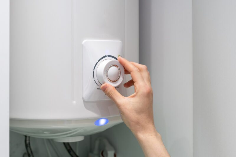 female adjusting temperature on bathroom electric boiler hanging on wall